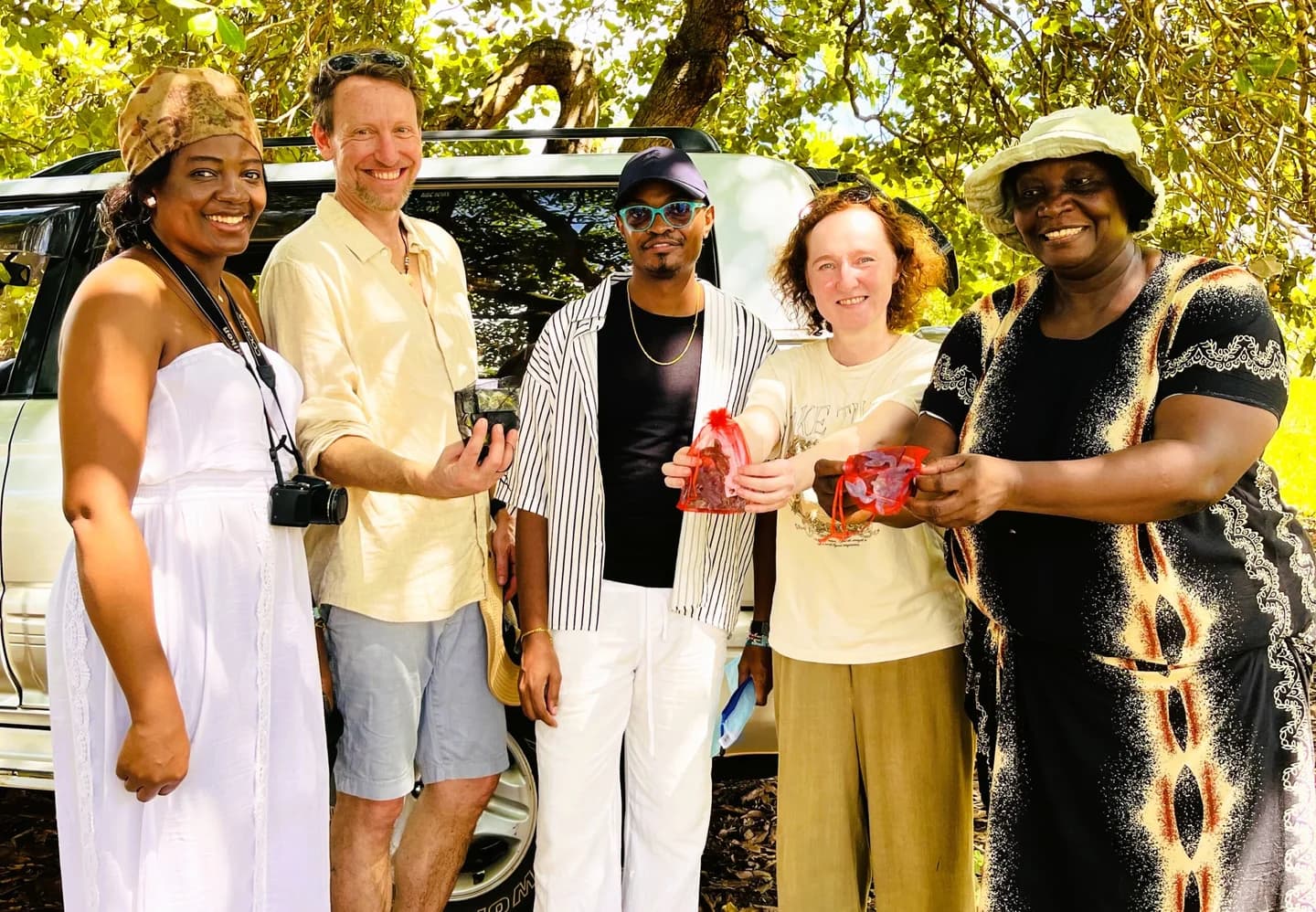 Five people gathered outdoors beneath trees during a community visit